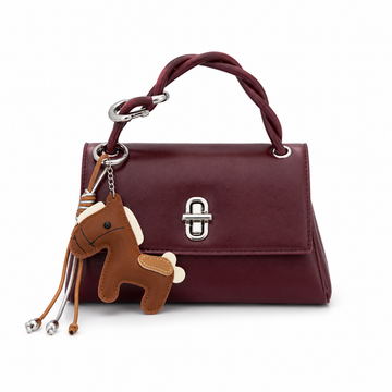 Burgundy structured top handle handbag with silver twist-lock closure and decorative brown horse charm on a white studio background.