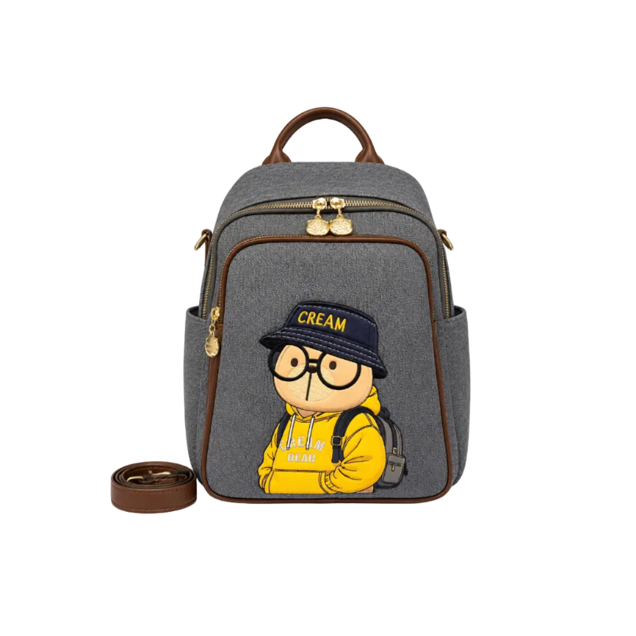 Gray Cream Bear backpack with an embroidered cartoon character wearing a yellow hoodie, gold-tone zippers, and a detachable shoulder strap.
