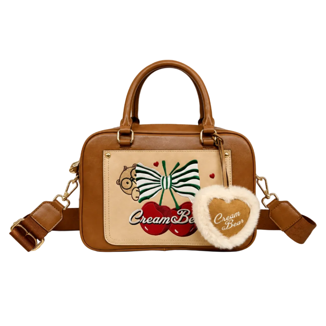Brown Cream Bear satchel handbag with embroidered bow and cherry design, plush heart charm, dual top handles, detachable shoulder strap, and white studio background.