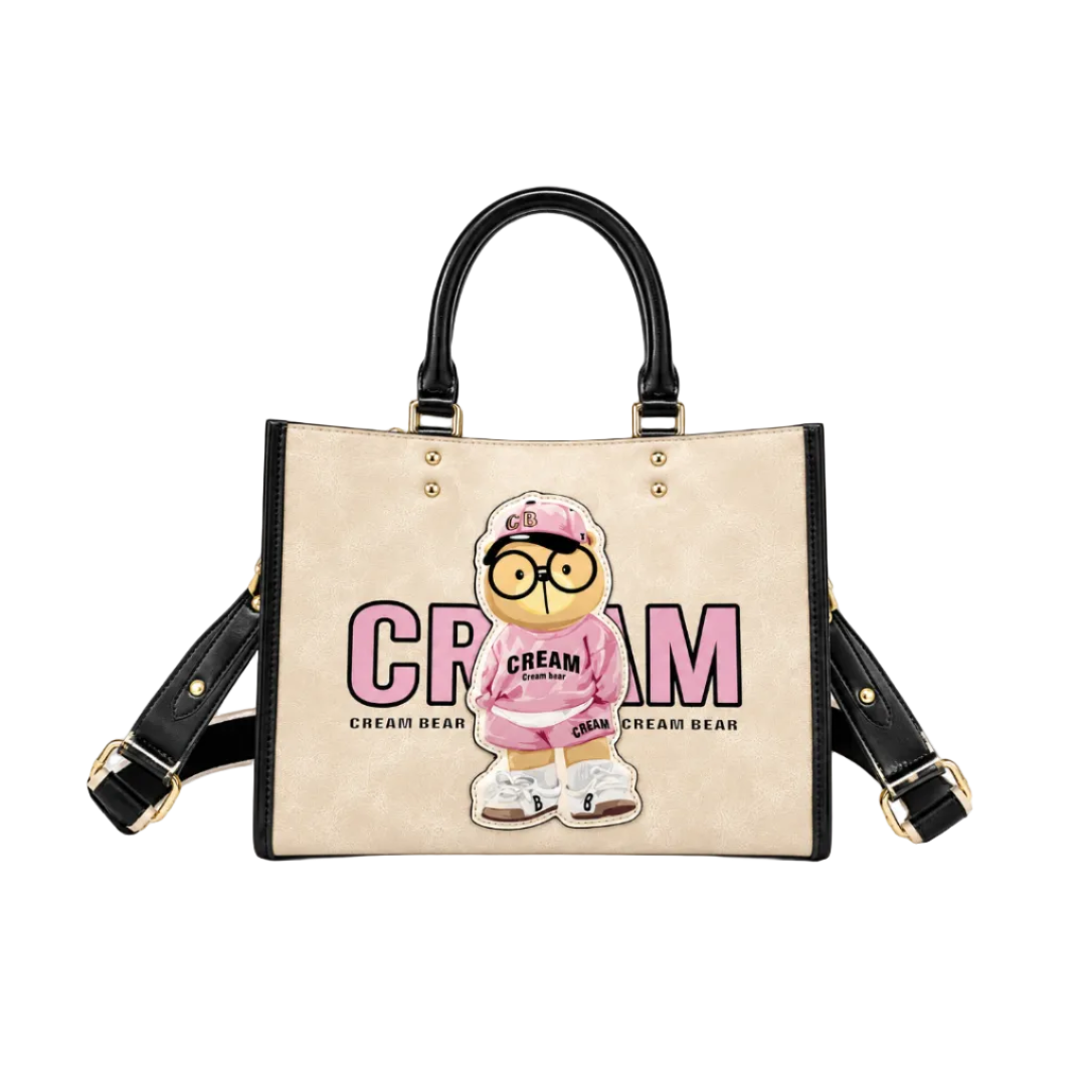 Beige Cream Bear fashion tote bag with black handles, pink bear graphic, gold hardware, and detachable shoulder strap on a white studio background.