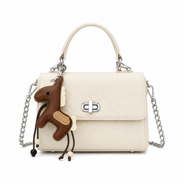 Front view of a white textured top handle handbag with a silver turn-lock closure, chain shoulder strap, and horse charm, photographed in a professional studio on a clean white background.