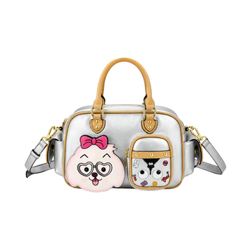 A silver metallic handbag with tan leather handles and trim, featuring two cartoon character patches on the front pocket and main body. One patch shows a pink dog face with heart-shaped glasses and a pink bow, and the other shows a black-and-white cat face with small colorful doodles.