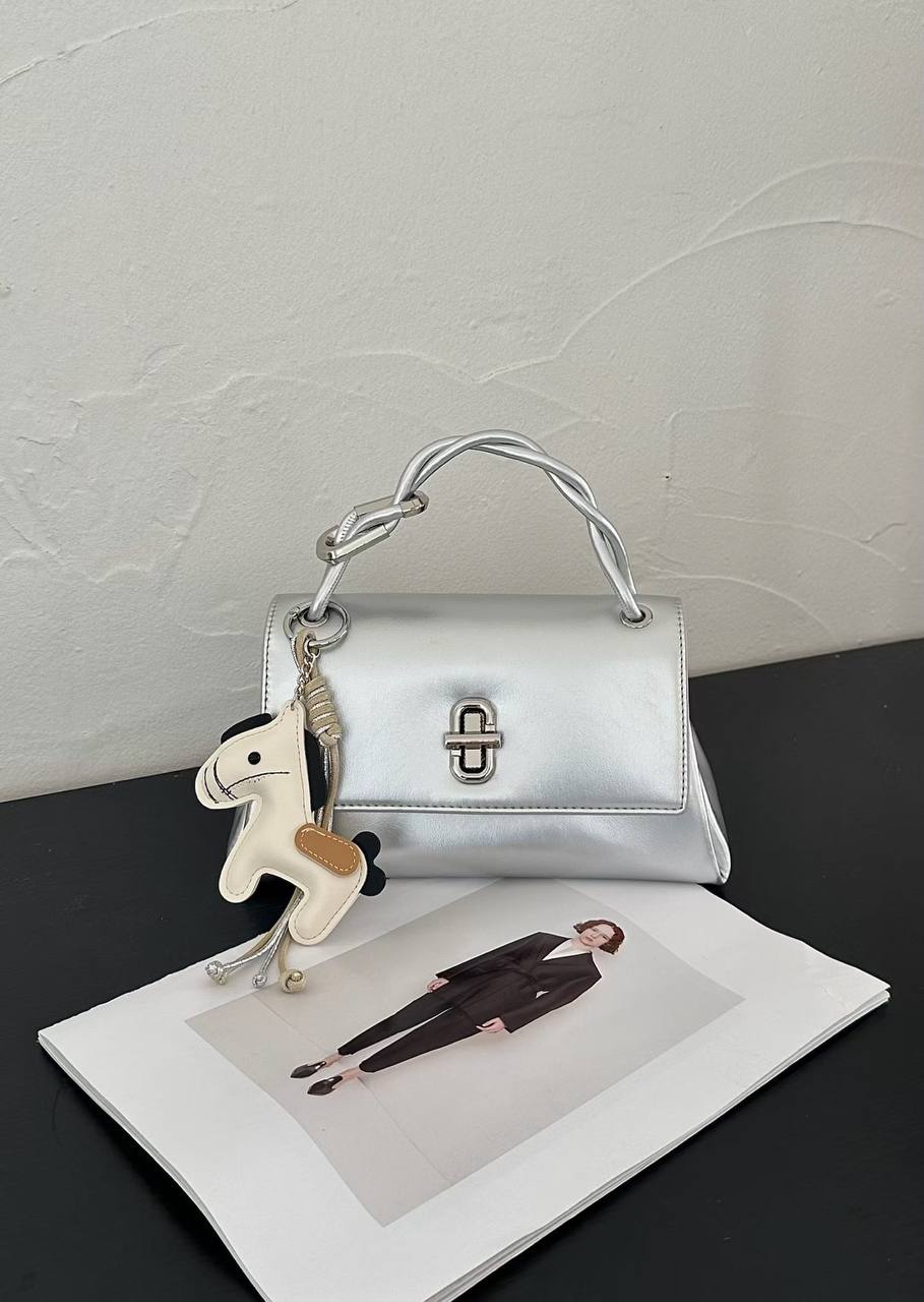 Metallic silver structured top handle handbag with silver twist-lock closure and decorative horse charm on a white studio background.