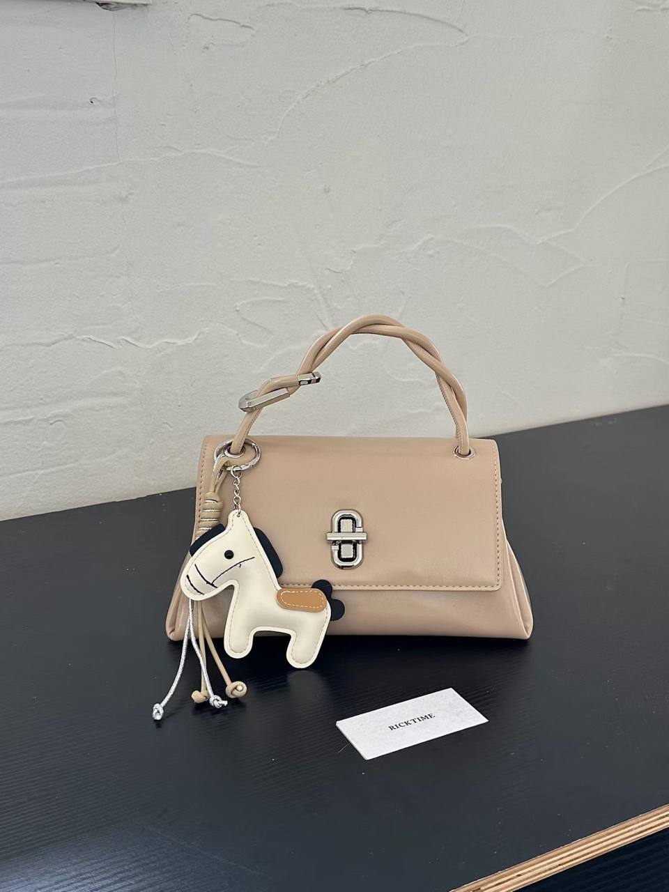 Apricot structured top handle handbag with silver twist-lock closure and decorative horse charm on a white studio background.
