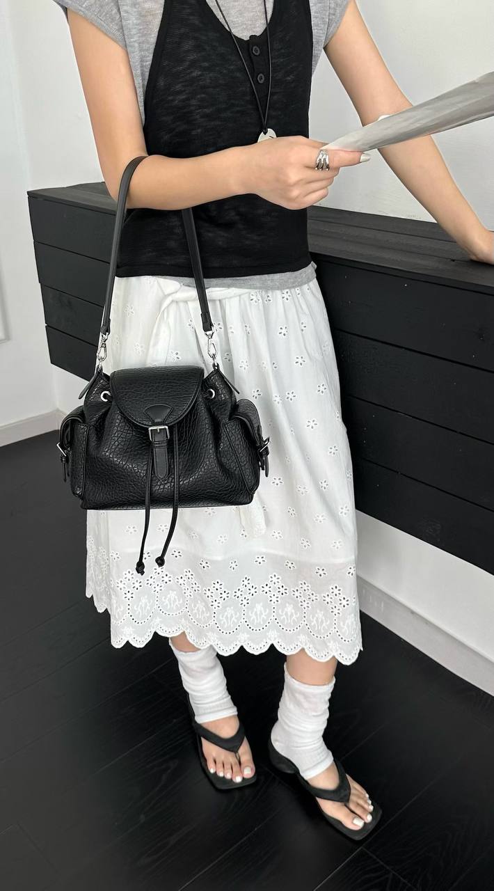 Black textured leather-look shoulder bag with flap closure, side pockets, adjustable shoulder strap, and detachable crossbody strap on a white background.